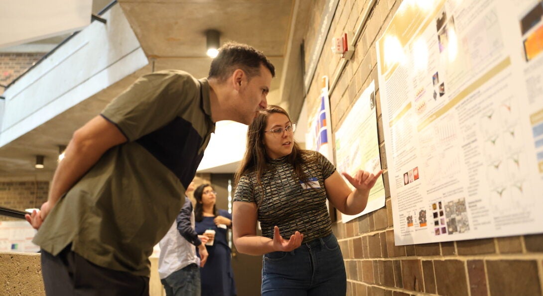 A man leans into look at a scientific poster while a woman explains the details.