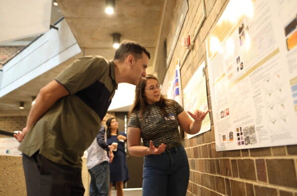 A man leans into look at a scientific poster while a woman explains the details.