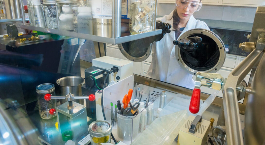 A female scientist in a lab coat pipettes behind lab equipment.