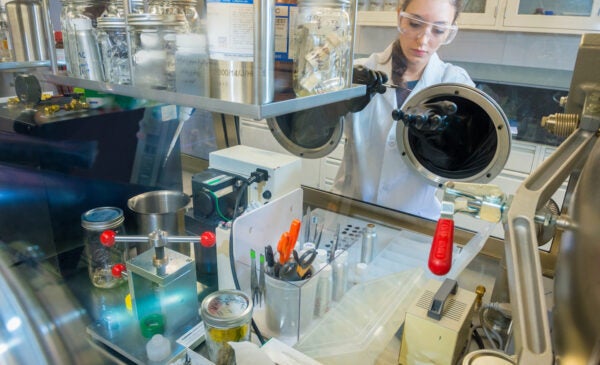 A female scientist in a lab coat pipettes behind lab equipment.