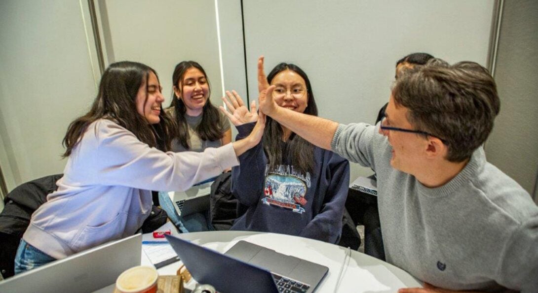 Students and a mentor high five over a table of laptops.