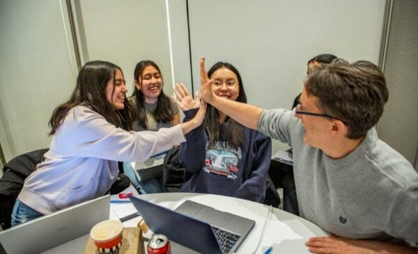 Students and a mentor high five over a table of laptops.