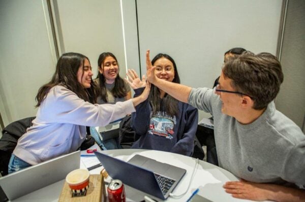 Students and a mentor high five over a table of laptops.