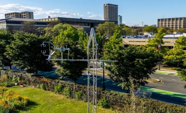 A metal tower with attached sensors in the foreground above a green field with UIC campus buildings in the background.