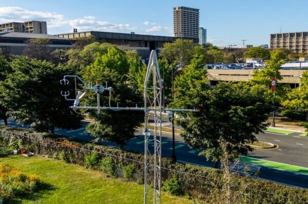 A metal tower with attached sensors in the foreground above a green field with UIC campus buildings in the background.